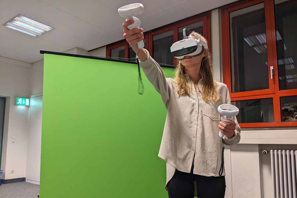 Eine Frau hat eine Virtual Reality Brille auf und steht vor einem Green Screen